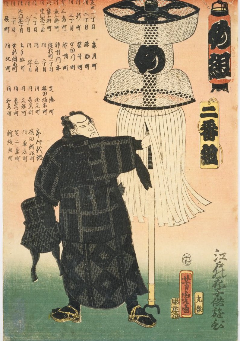 歌川芳虎「二番組め組」。格子縞の半纏を着た男が、黒い巴模様の球形を頂いた大きな纏を肩に担いで立つ。背景左側には、め組の受け持ちである芝一帯の細かい町名が縦書きでびっしり並ぶ